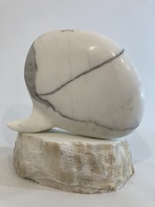 Stargazing. 40x35x20. Carrara statuary marble. Stargazing reflects on the stillness and being of laying back and gazing at the night sky. There is a rock formation where I live that inspired me. Stone is of the earth but holds the ancient histories of the universe in its minerals. The veining of the marble somewhat resembles a galaxy or gas clouds. The head is simplified to the point of it being just a large pebble.
